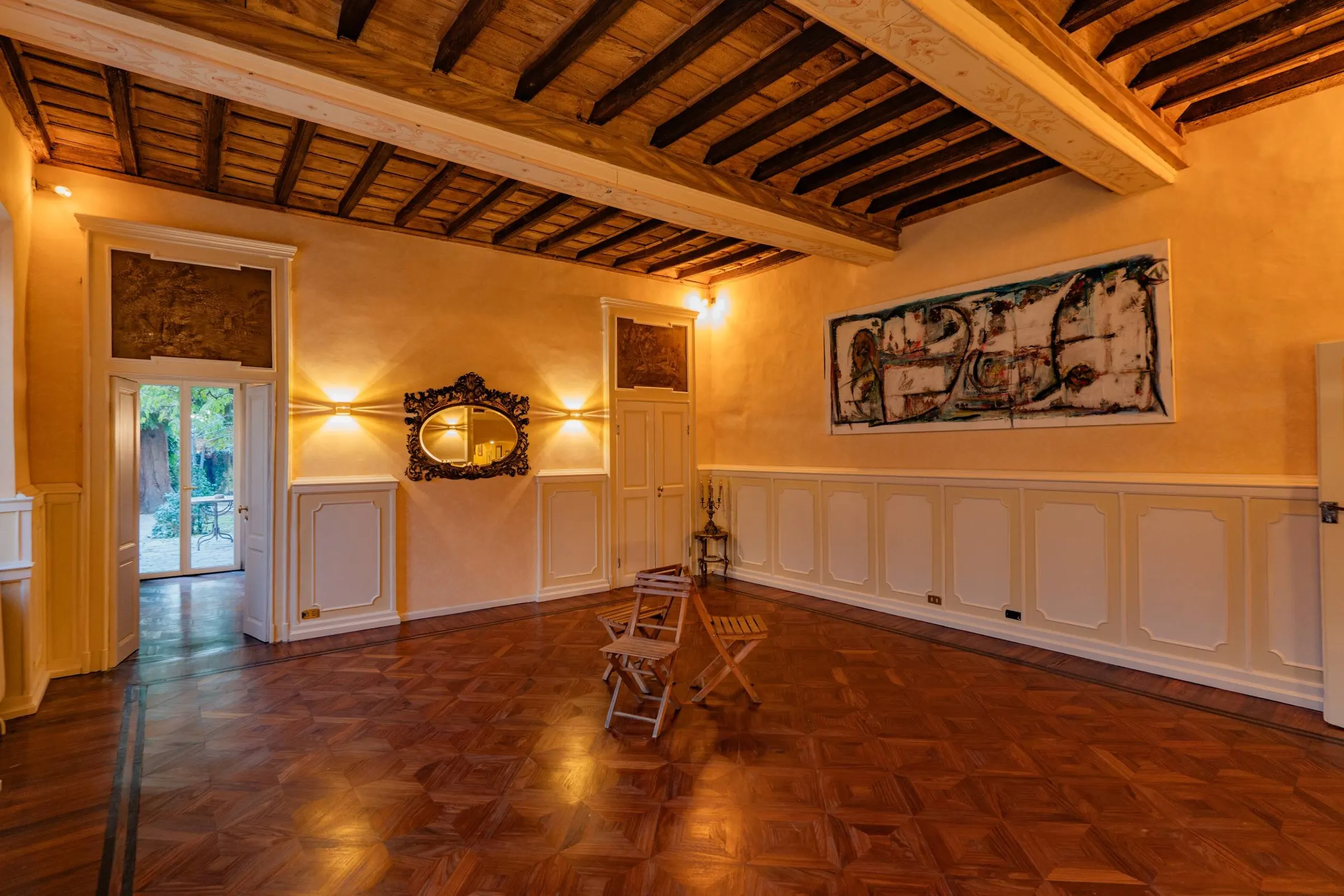 La sala antica senza allestimento: il parquet a riquadri, la boiserie chiara e la sovrapporta dipinta