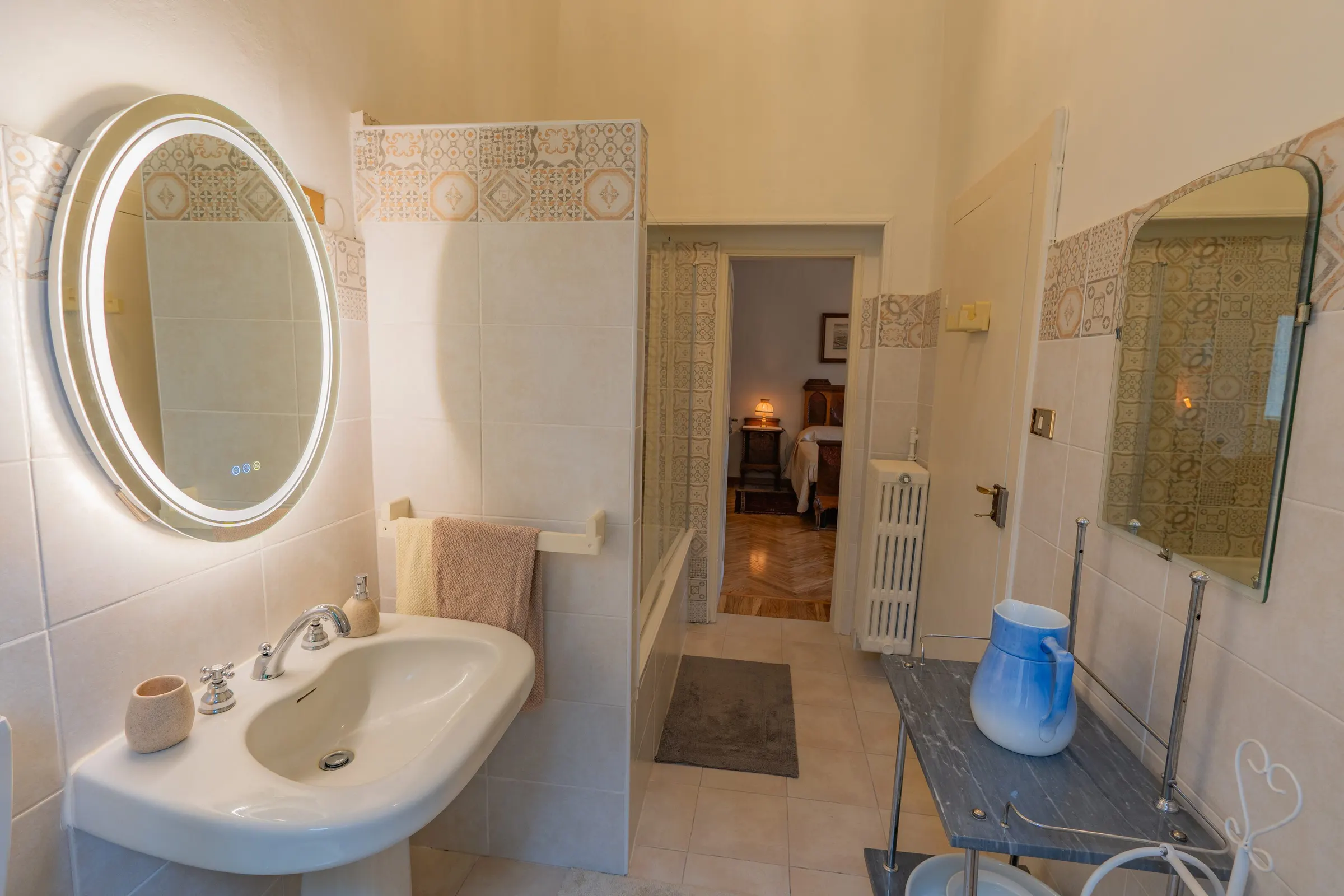 Il bagno chiaro, con il lavabo, lo specchio ovale illuminato e le piastrelle decorate
