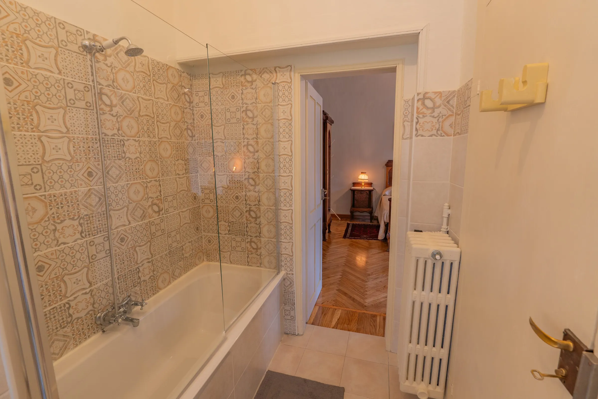 La vasca con la doccia e il vetro nel bagno chiaro, con la porta aperta sulla camera