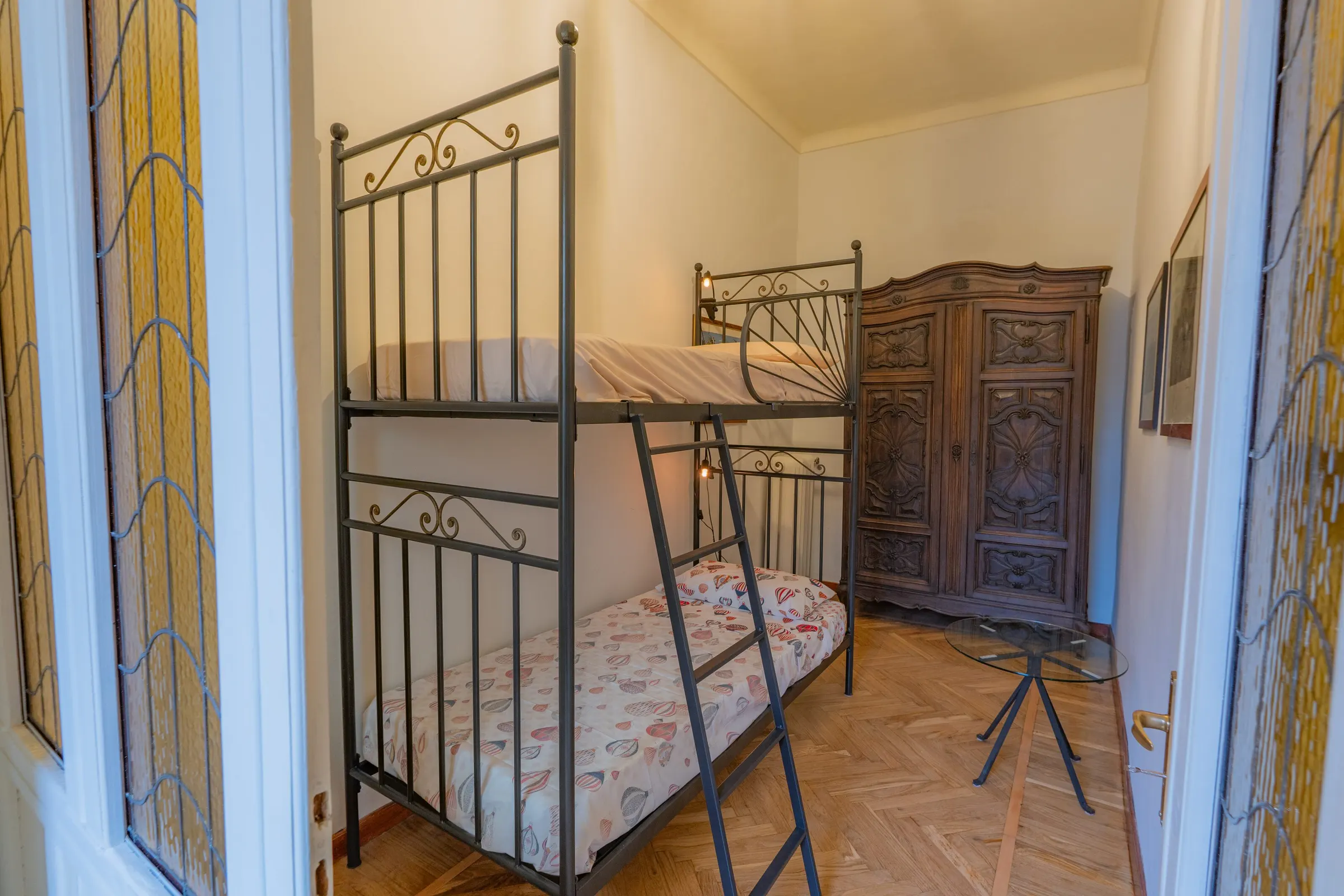 Il letto a castello e l’armadio antico di legno scuro, con le porte a vetri policromi sulla sinistra