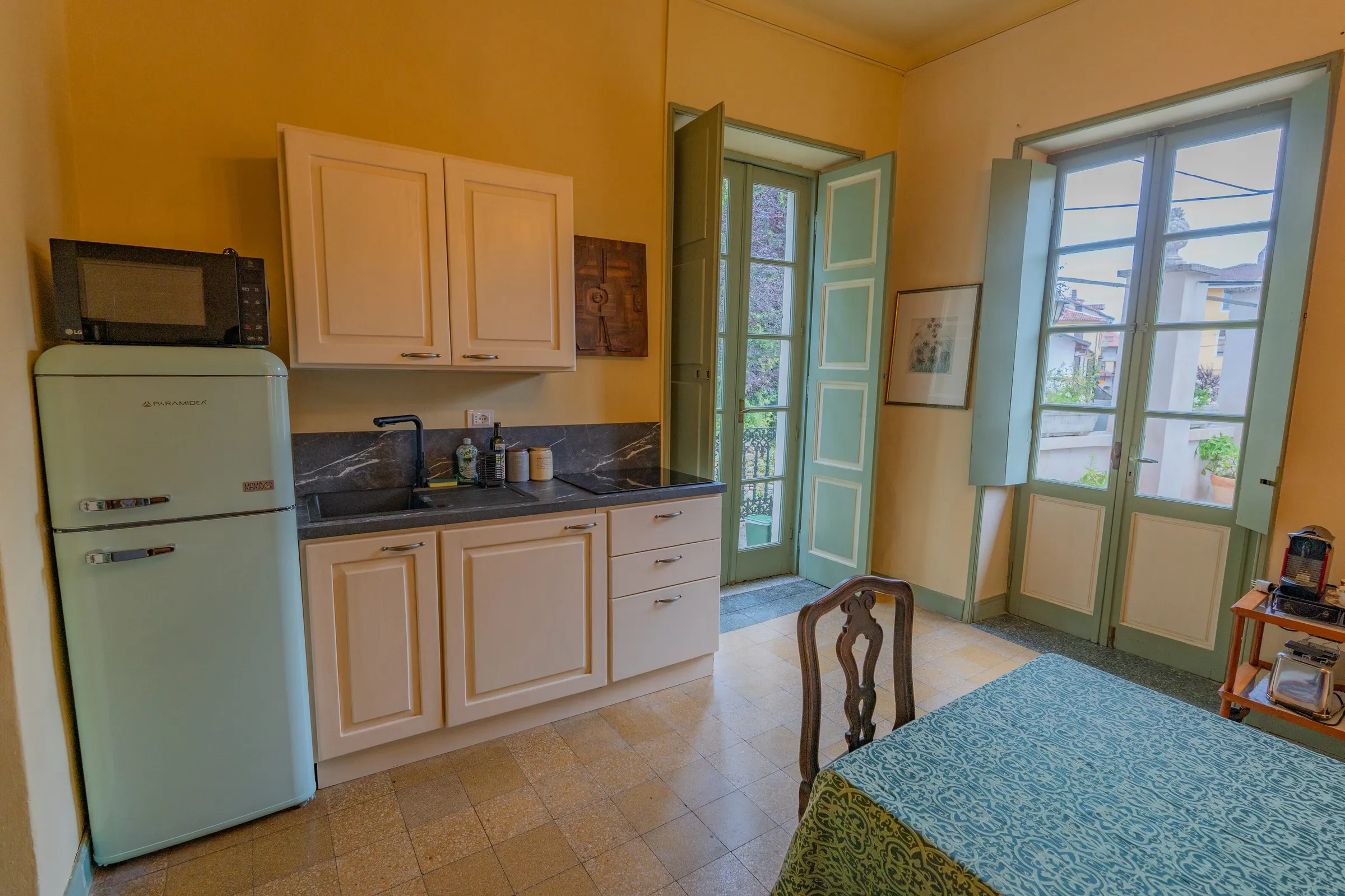 L’angolo cottura, con i pensili bianchi, il frigorifero verde menta di foggia vintage e il piano di lavoro scuro sotto la finestra