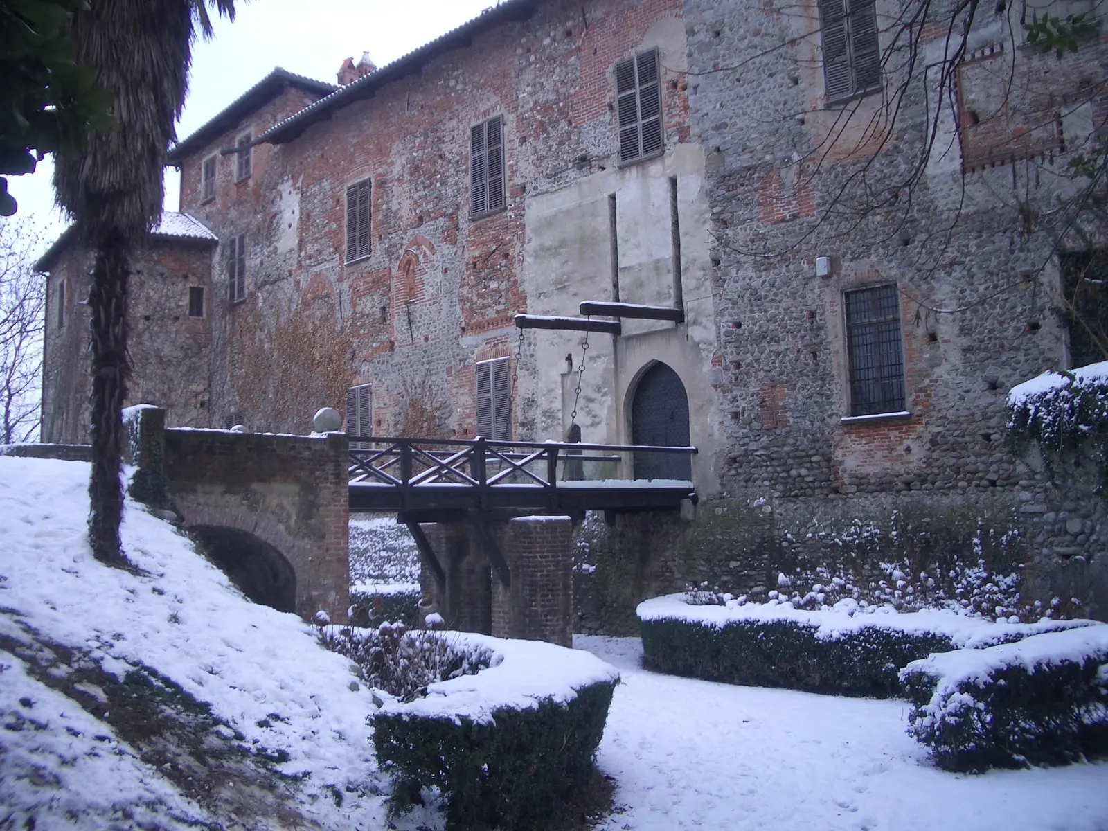 L’ingresso del Castello di Malgrà d’inverno, con il ponte di legno sul fossato, i muri di mattoni e le siepi coperte di neve