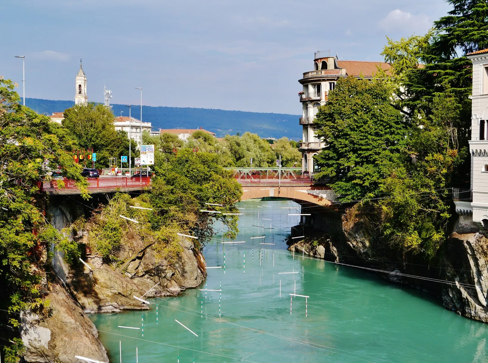 La Dora Baltea a Ivrea, verde e trasparente fra le rocce, con le porte dello slalom sospese sull’acqua e un ponte sullo sfondo