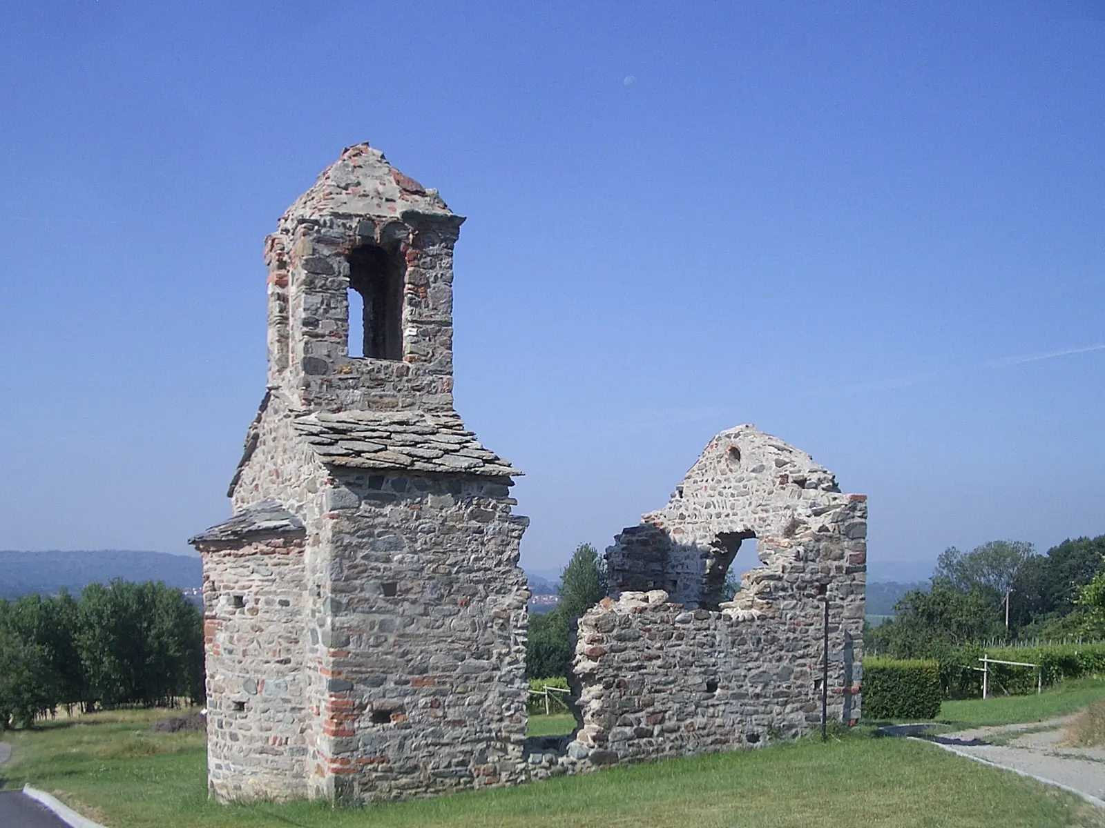 Le rovine del Gesiùn, con il campanile di pietra e i muri della navata, su un prato sotto il cielo azzurro