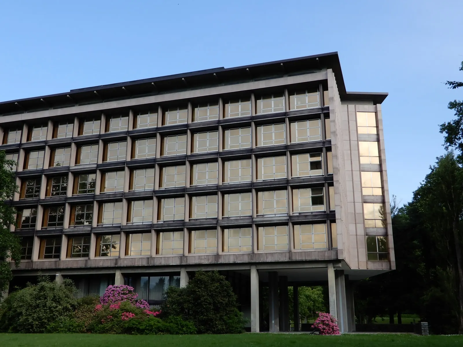 Il Palazzo Uffici Olivetti a Ivrea, la facciata di vetro e pietra sui pilastri, con le azalee in fiore davanti