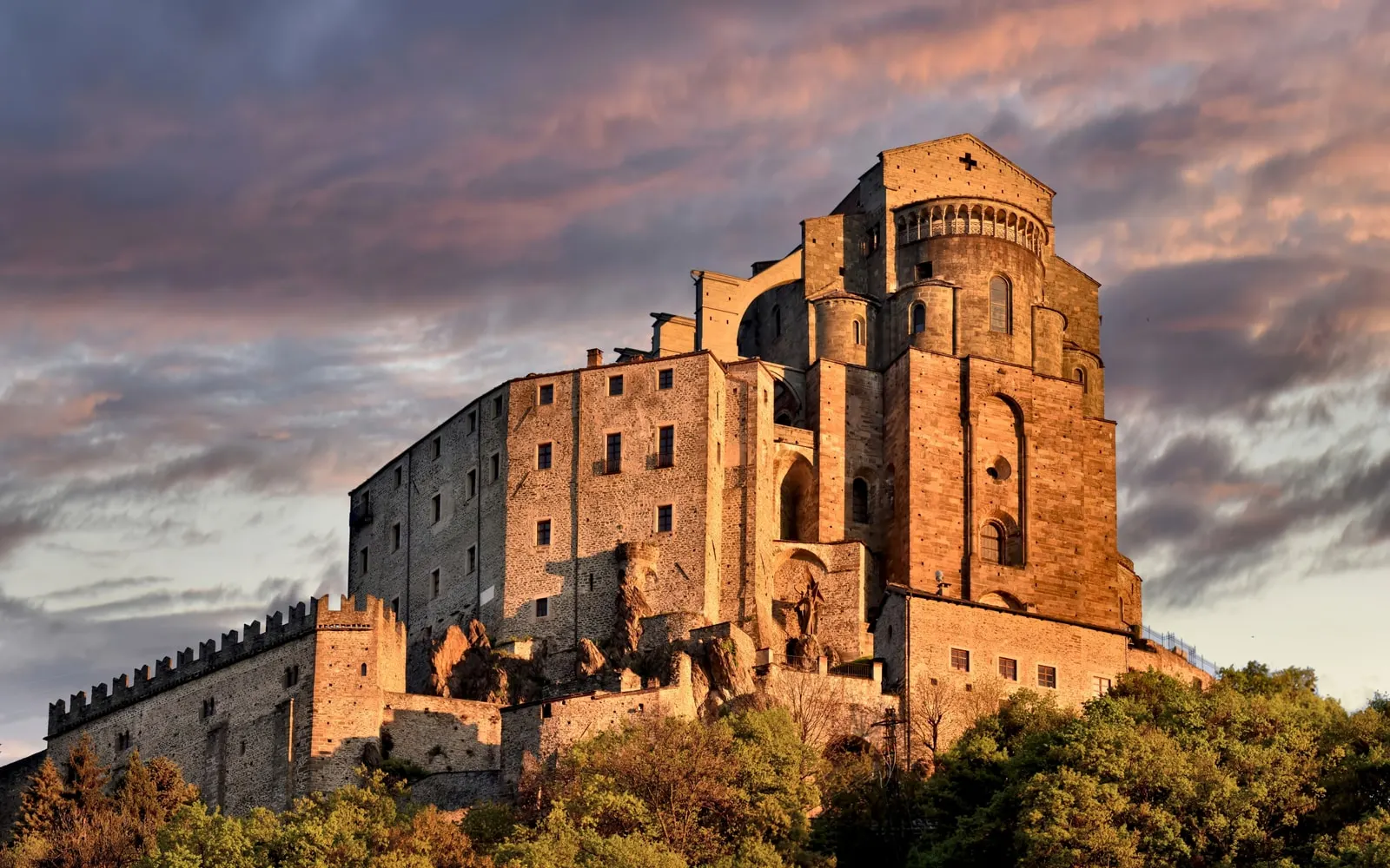 La Sacra di San Michele in cima al monte, accesa dalla luce rosata dell’alba